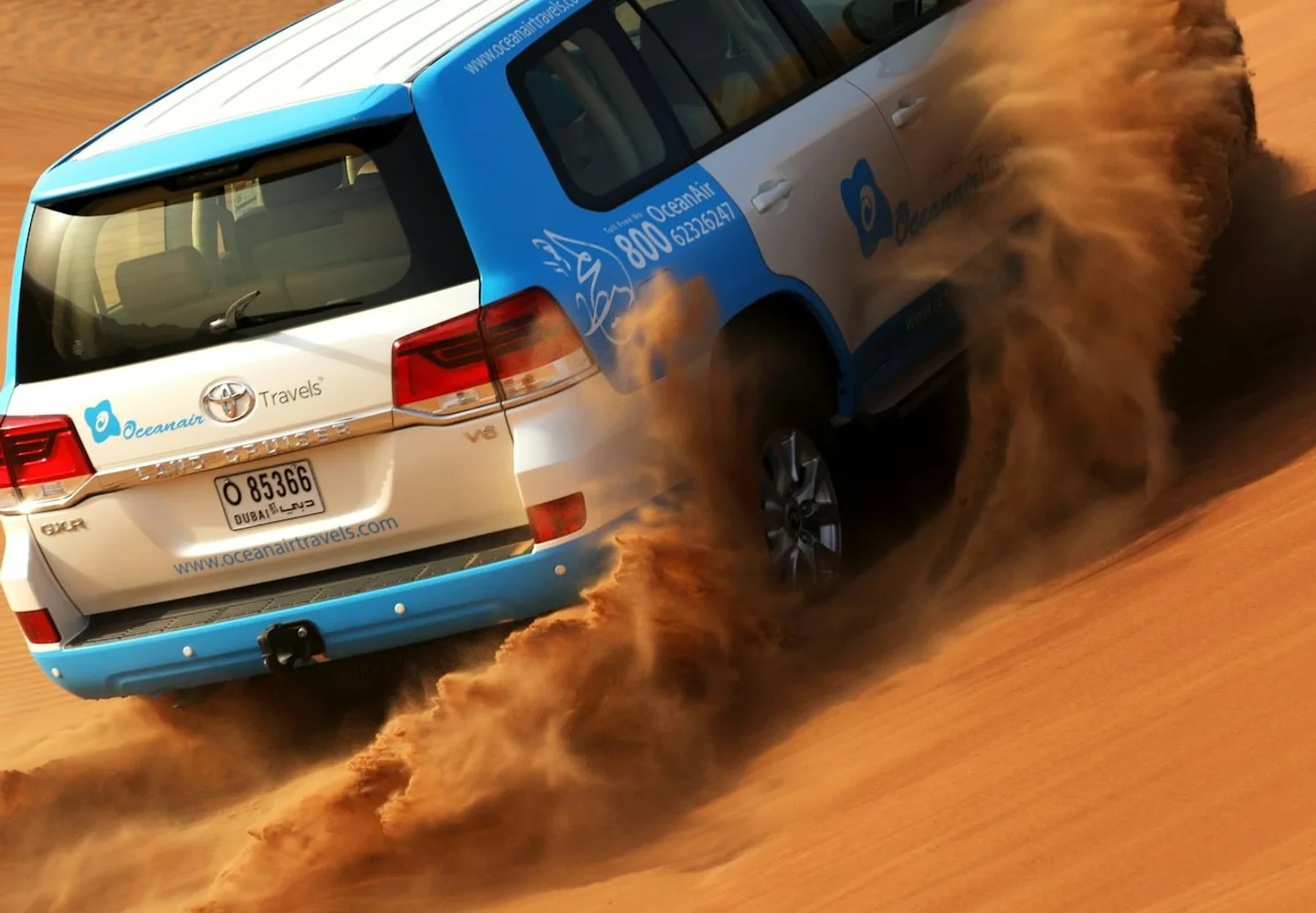 Blue four-wheel-drive vehicle driving across Dubai sand dunes